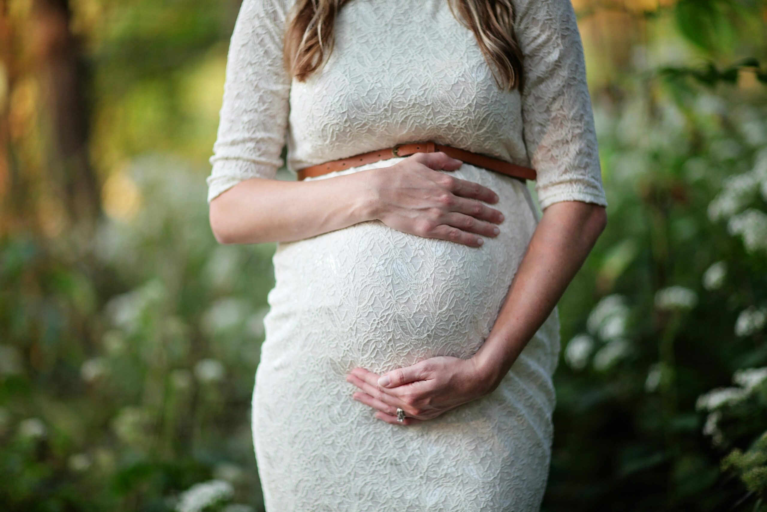 A pregnant woman in a lace dress gently cradling her belly in an outdoor setting.